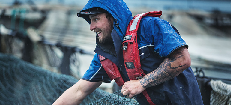 A man in wet weather gear and a life jacket hauls in fishing nets.