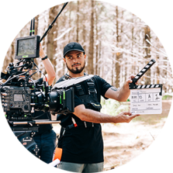 Person with film clapper board in forest in front of camera.