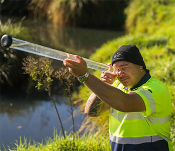 Worker wearing a high-viz looking into a large test tube filled with river water to assess the water quality. 