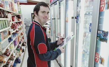 Photograph of Patrick Green working in local supermarket standing in supermarket aisle with a clipboard.
