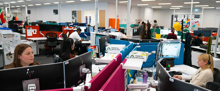 A large open plan office with people working at desks on computers.