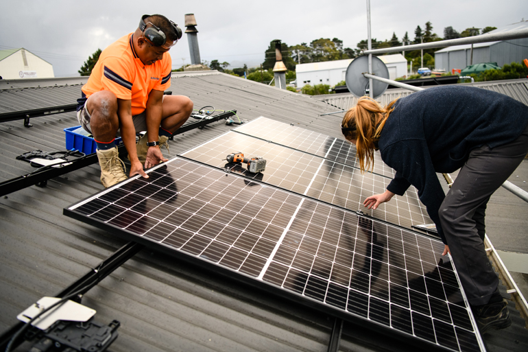 Two people on a roof installing solar panels. 