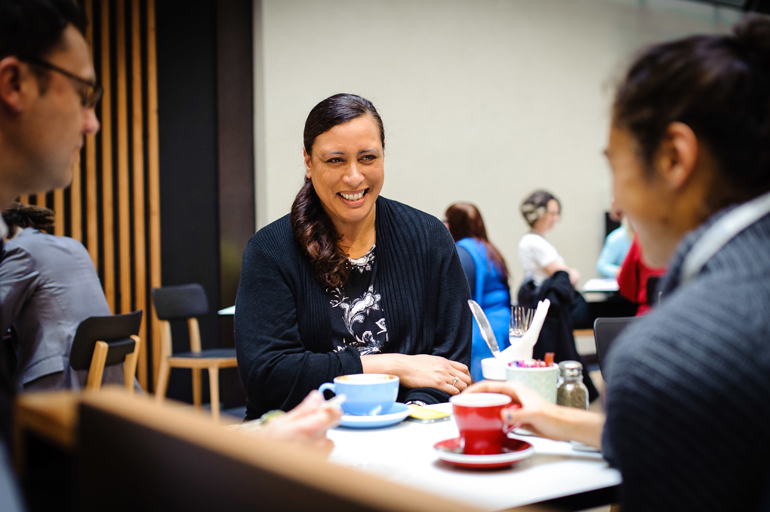 Group of three people talking and drinking coffee.