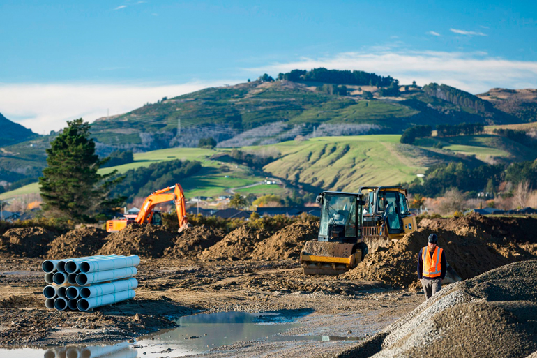 A person in hi-vis and heavy machinery at a construction site. 