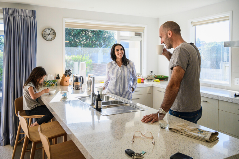 A family in their home gathered around a kitchen counter and eating breakfast. 