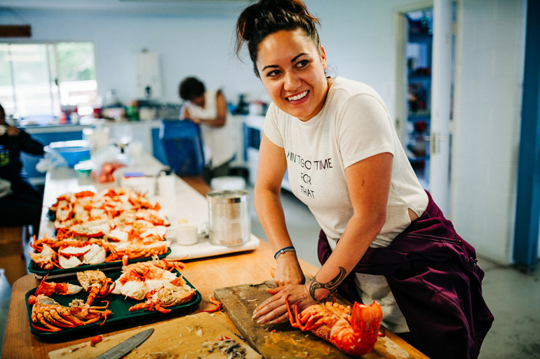 Female presenting person chopping up a crayfish on a counter with other trays of crayfish.