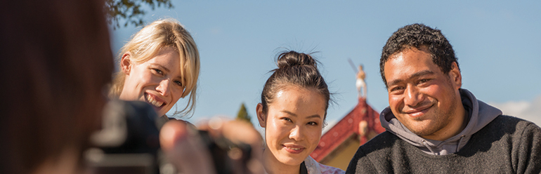 Decorative image: three people having their photo taken on a marae.