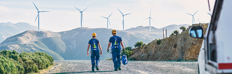 Decorative image: two people in climbing harnesses and helmets walking toward five wind turbines.