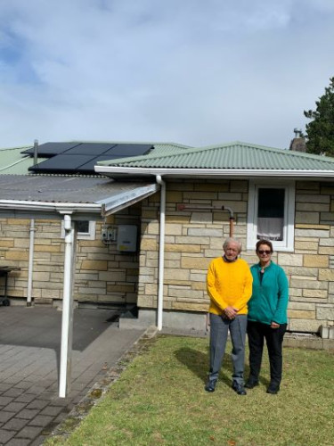 2 people stand outside of a home with rooftop solar panels.