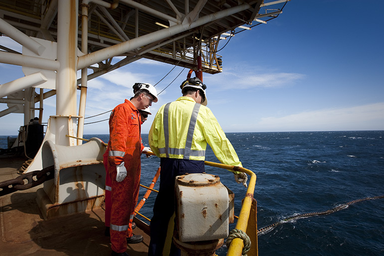 Three men standing at the railing of an oil rig at sea