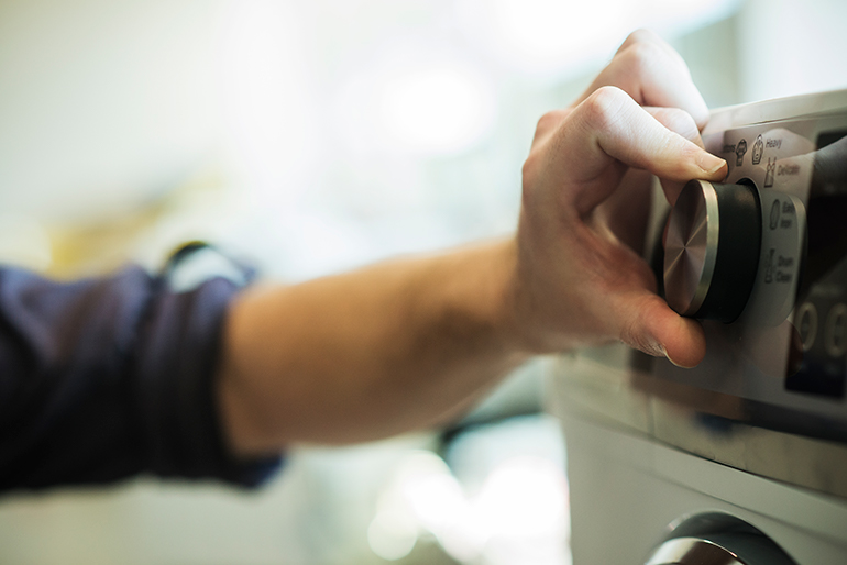 A hand turning a dial on the front of a washing machine