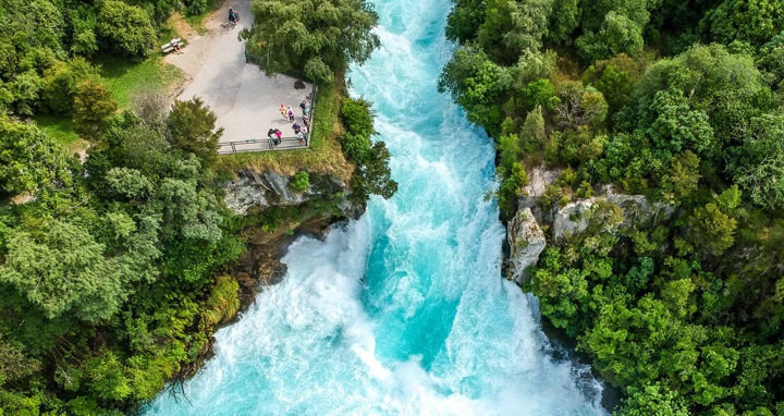 Photo: The Huka Falls from above. The water is flowing strongly and there are lush trees on either side.