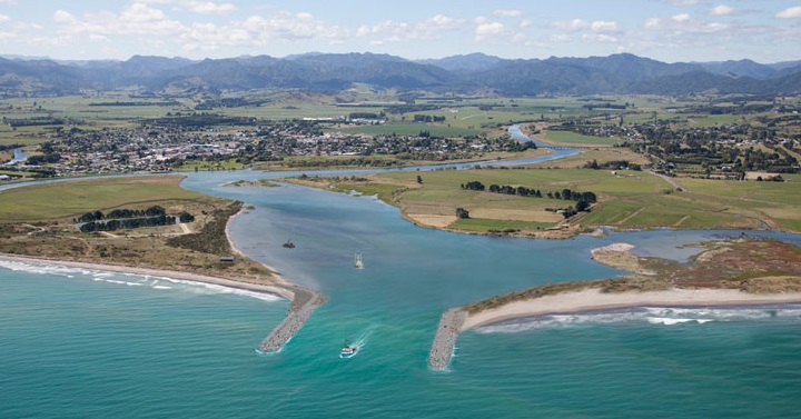 Photo: The Ōpotiki Harbour mouth with a boat sailing in the middle of it. A mountain range is in the distance. 