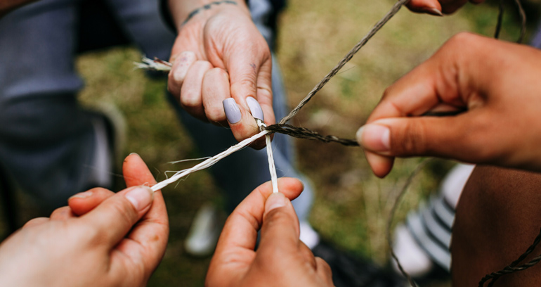 Photo of different hands holding joined plaited string