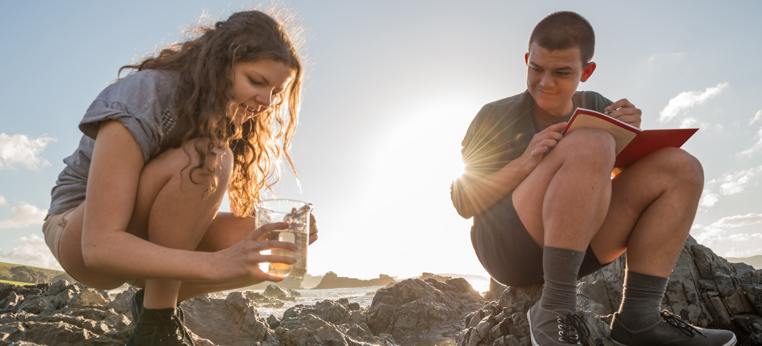 Two school children taking sample of water and recording it.