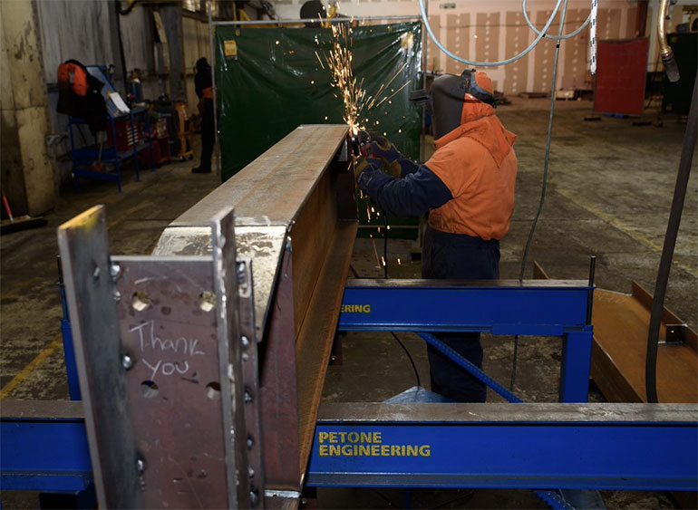A worker in safety gear welding a steel beam.