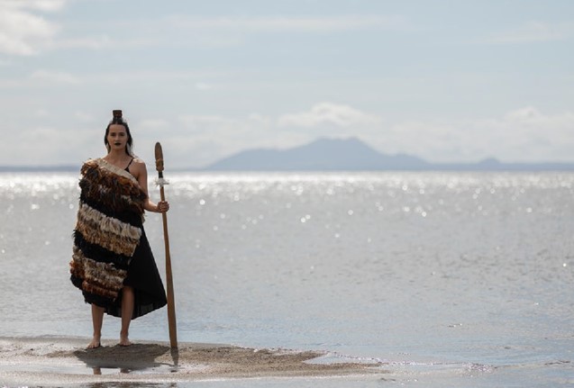 Young Wahine on beach wearing a Korowai and holding a taiha