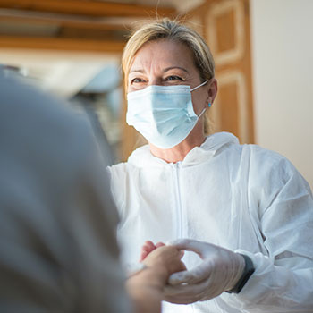 A masked female health worker holds a patient’s hands