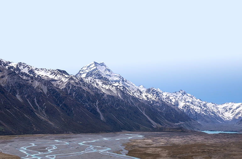 Snow covers a steep mountain range with a braided river in the foreground