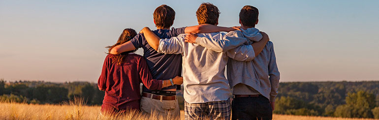 Four youth stand with their arms around each other looking towards the horizon 