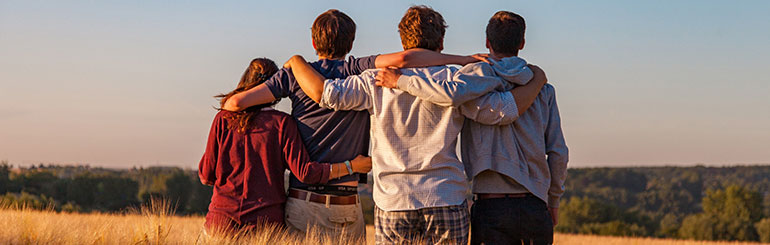 Four youth stand with their arms around each other looking towards the horizon