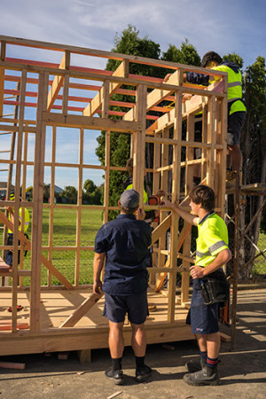 Backs of teacher and student working on building a house frame  