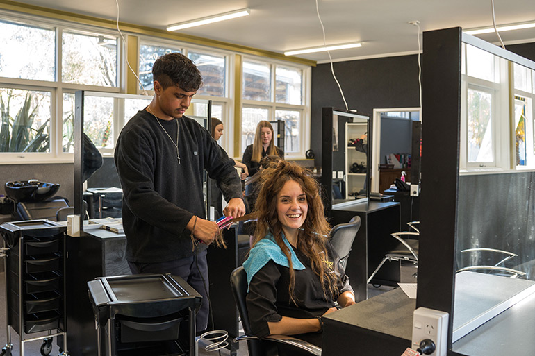 Young man straightening the hair of a young woman who is sitting down.