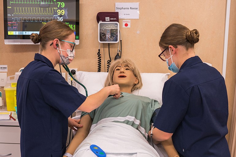 Two young women performing a medical exam on a dummy.