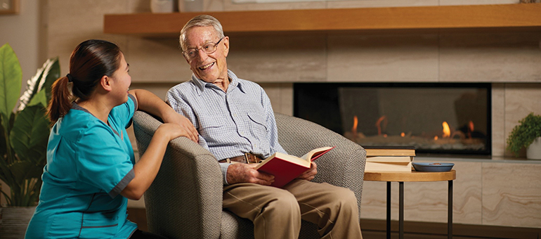 An elderly man talks with a caregiver in the lounge area of a retirement village.