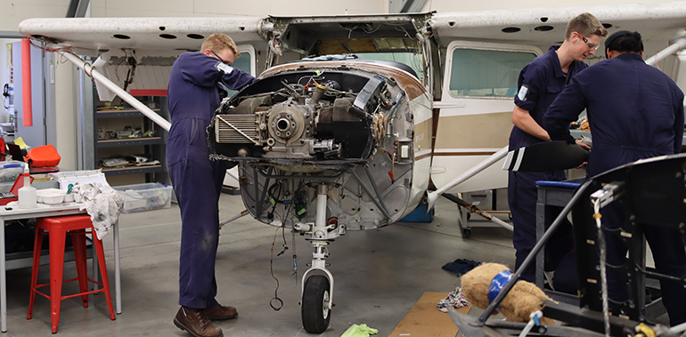 Three young men working on a light aircraft with the front propeller removed.