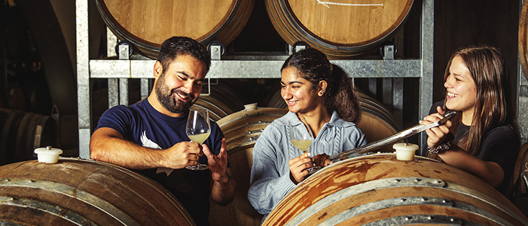 Three co-workers tasting wine surrounded by wine barrels.