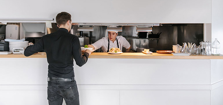 A person collecting a meal order from a hatch to the cafe kitchen.