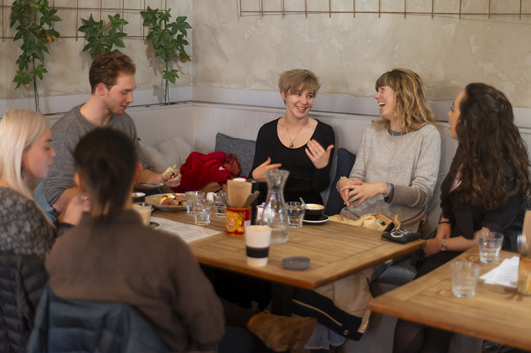 A group of young people seated at a café table drinking coffee.