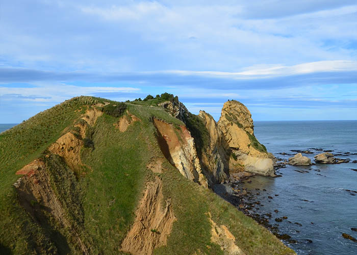 The steep, rocky slopes of Huriawa Peninsula surrounded by sea and fallen boulders