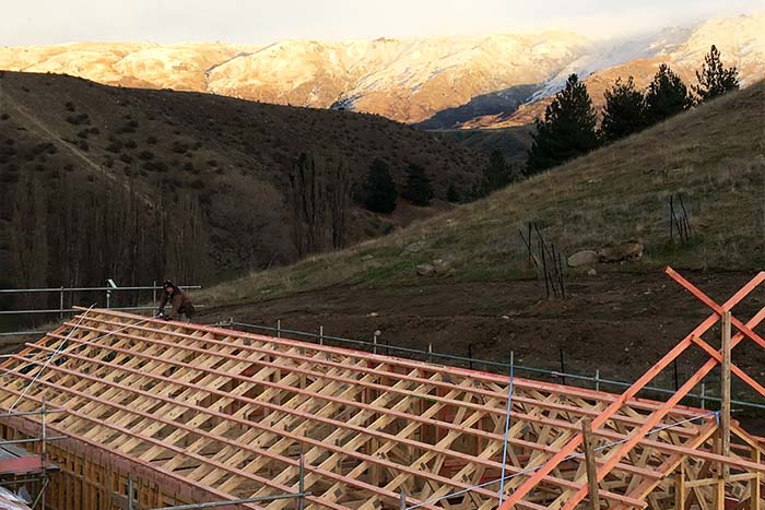 A man working on the frame of a house with hills in the background
