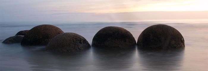 A cluster of dark round boulders surrounded by sea at dawn