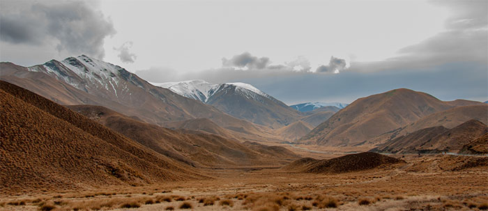 A wintry view of Lindis Pass with hills covered in tussock and snow-capped mountains