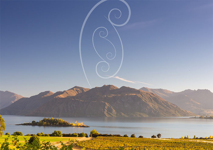 Morning sun on a vineyard with Lake Wanaka and mountains in the background. A kaponga or silver fern is shown in the sky.