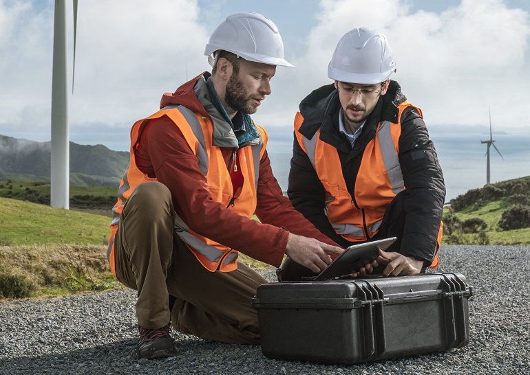 Picture of two men looking at a tablet with wind turbines in the background.