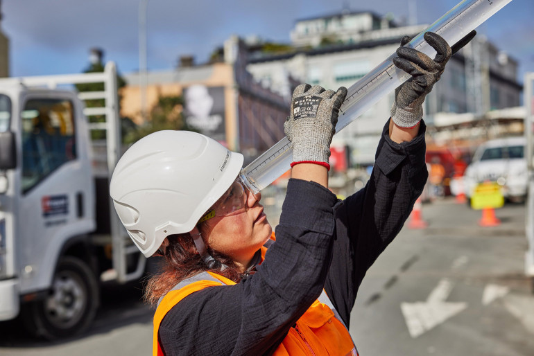 Woman wearing hi vis vest and helmet and looking through cylandir