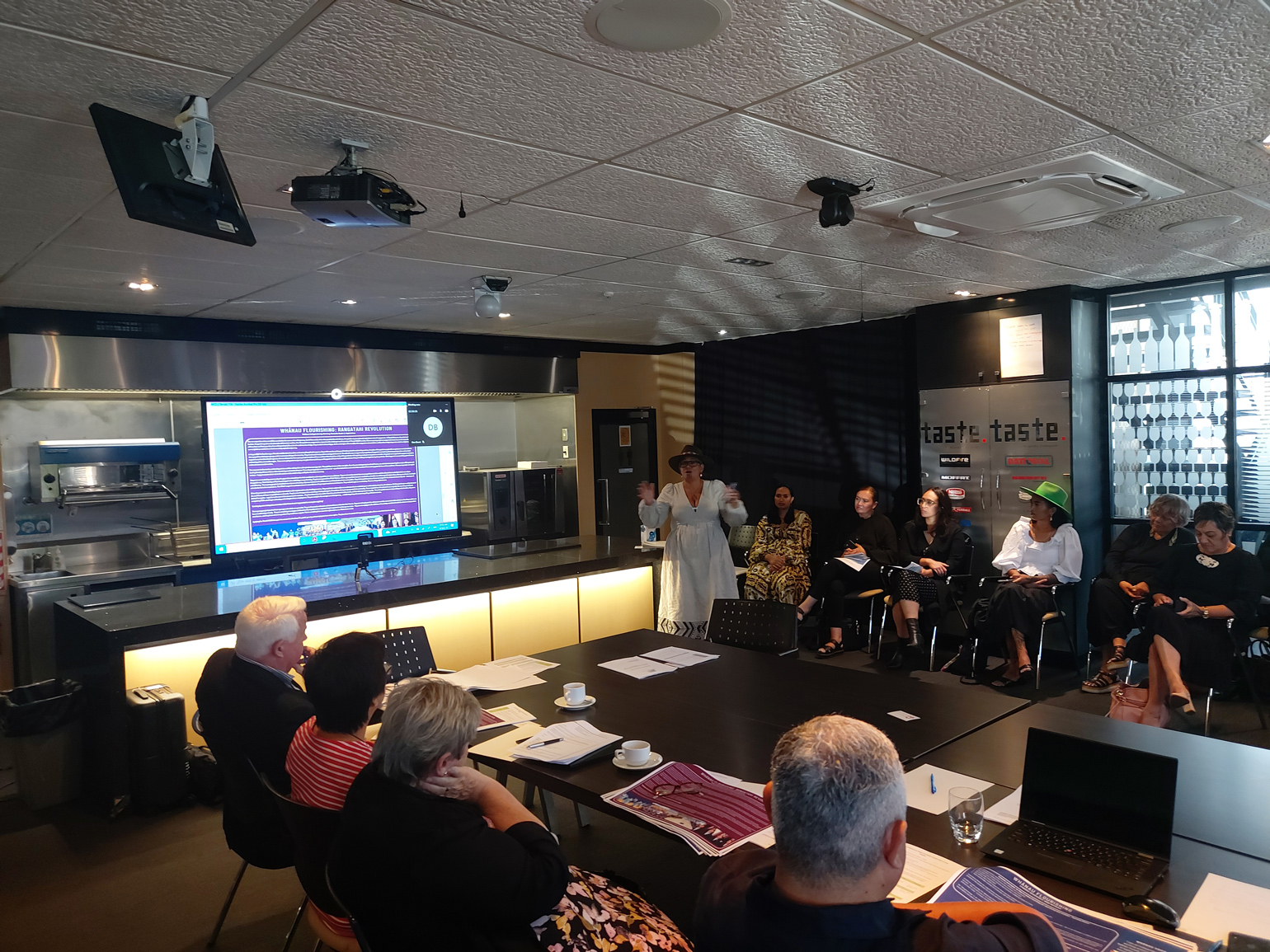 Woman with moko kauae presenting to people sitting at a table