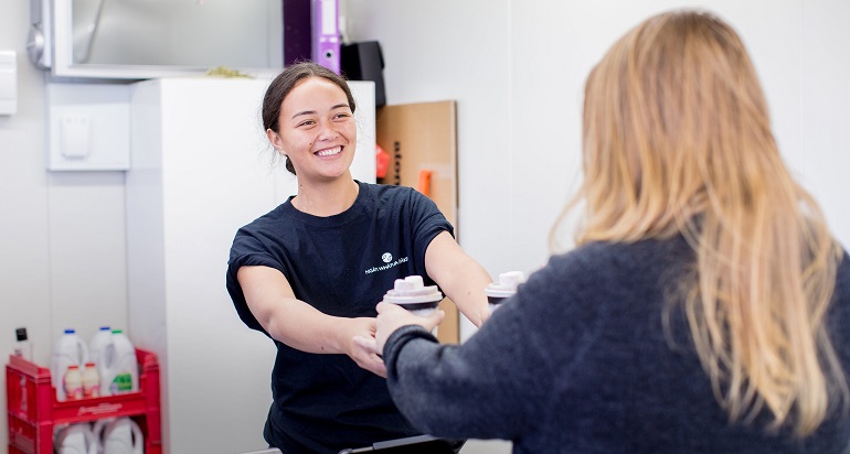 A young woman serving coffee to a customer with a smile.