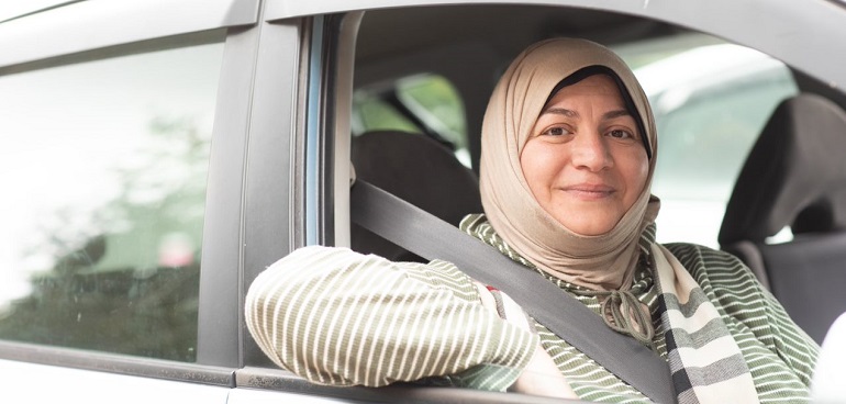 A woman driver in a hijab looks through an open car window.