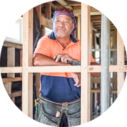 Mature construction worker peering through framing timber.