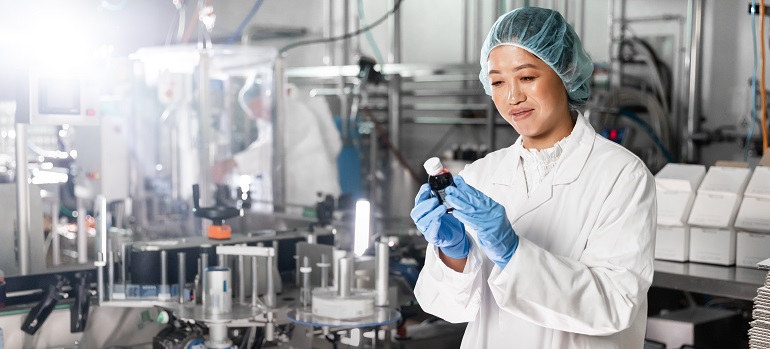 Woman in factory in lab tech clothing looking at a bottle of liquid.