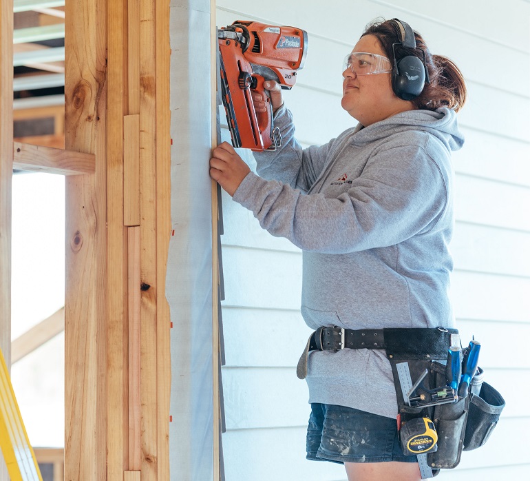 Women with nail gun nailing door frame.