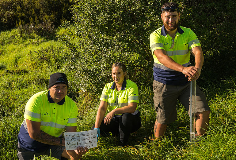 3 workers outdoors in grass with water testing equipment.