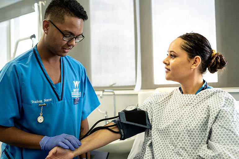 Male nursing student checking the blood pressure of a female patient. 