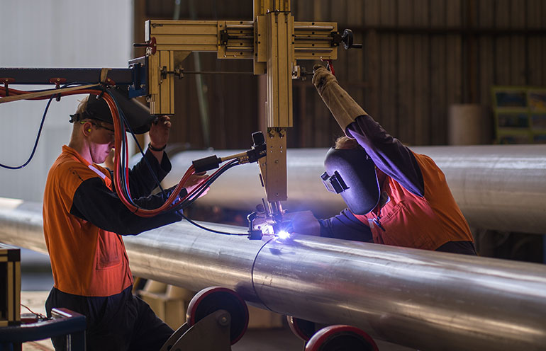 Two young people welding a pipe.