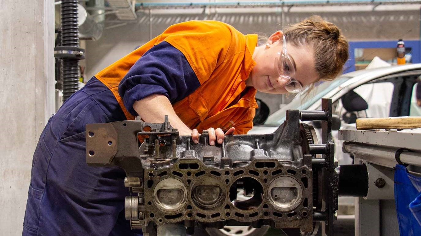 Photograph of Tai Poutini Polytechnic female student in overalls working on a car engine.